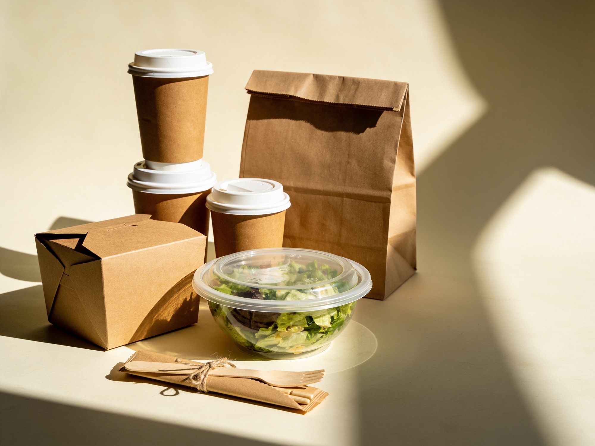 Kartonnen koffiebekers met deksel, een maaltijdbox, een saladebak, houten bestek en een papieren tas